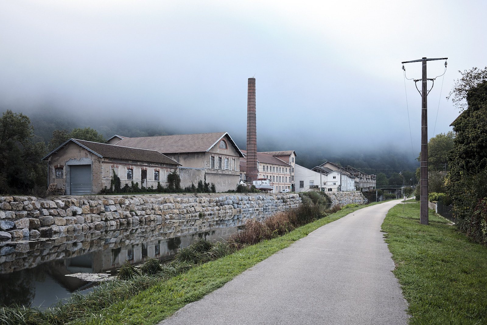 Die ehemalige Papierfabrik in Deluz am Kanal unter nebligem Himmel